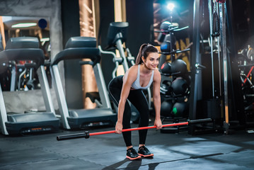 Young fit woman exercising with weighted workout bar in the gym.