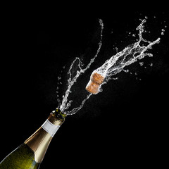 Opening a bottle of champagne. The celebration theme with splashing champagne isolated on black background. Traffic's flying.