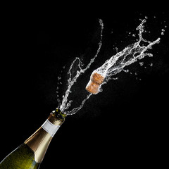 Opening a bottle of champagne. The celebration theme with splashing champagne isolated on black...