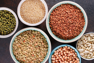 Top view on bowls with various raw grains and seeds on a textured dark background.