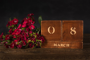 International Women’s Day vintage wooden Perpetual calendar for March 8 on a black background and a bunch of red carnation flowers