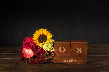 International Women’s Day vintage wooden Perpetual calendar for March 8 on a black background and a bunch of various flowers