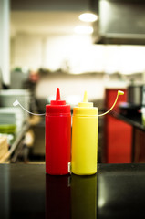 plastic containers for ketchup and mustard sauces together seems that they are waving in the kitchen of a restaurant