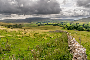 storm clouds gathering over a valley of farm land in Yorkshire, England. Handmade stone wall. Sheep grazing. 
