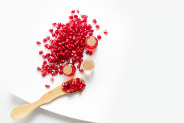 Pomegranate oil in a bottle and pomegranate seeds on a white background