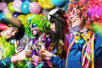 Lachende Freunde in bunten Kostümen trinken Sekt bei einer Karneval party .