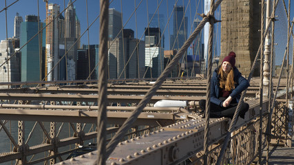 Young and reckless girl sits on the rim of Brooklyn Bridge New York