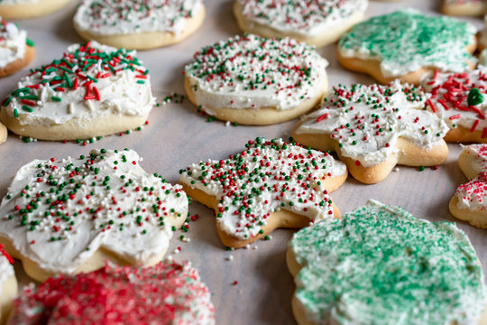 Various sugar cookies on parchment paper.  Frosted with white icing and sprinkled with various christmas decorative sugars.