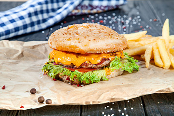 Fresh homemade burger with meat, sauce and vegetables on on wooden background. Close up view on american fast food. Restaurant, food menu, recipe, cafe concept. Lifestyle with copy space