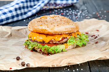 Fresh homemade burger with meat, sauce and vegetables on on wooden background. Close up view on american fast food. Restaurant, food menu, recipe, cafe concept. Lifestyle with copy space