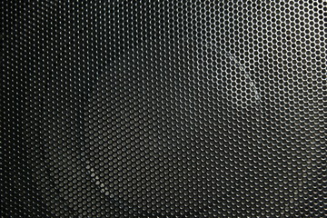 The speaker of a musical column hidden behind a grid with a pattern of rhythmically arranged holes