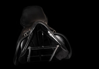 Black leather professional jumping saddle at stand at black background. front view