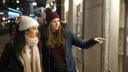 Two girls on a shopping trip in New York walk along shop windows