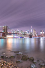 Fototapeta premium View on Financial district and Brooklyn bridge at night from East river beach with long exposure