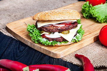 Double Burger with meat, sauce and vegetables on on wooden background. Close up view on american fast food. Restaurant, food menu, recipe, cafe concept. Lifestyle with copy space