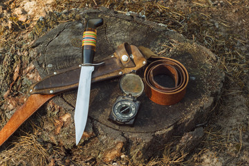 Hunter knife, leather sheath, belt and army compass. Composition with hunting equipment in the woods