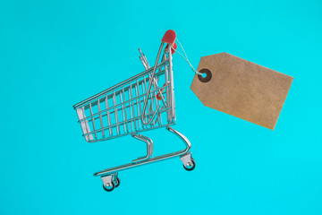 Shopping trolley toy with special offer tag on turquoise background minimalistic flat lay concept.