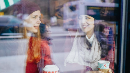 Two friends drink coffee in a cafe with a view to the street