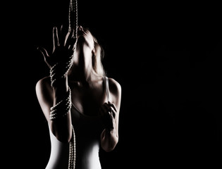 Beautiful slender blonde girl with big breast and nipples appearing through clothes, wearing a white bodisuit, sensually plays with the ropes on black. Artistic noir silhouette photo