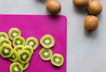 Ripe cut kiwi on pink plastic bard. Gray background.