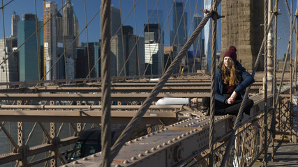 Fototapeta na wymiar Young and reckless girl sits on the rim of Brooklyn Bridge New York