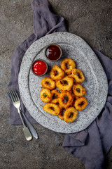 Fried squid rings on gray stone plate with sauces. Gray concrete background