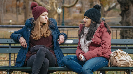 Two girls sit on a bench on Central Park enjoying their time in New York