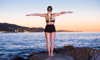 Young female is meditating on a rock near sea
