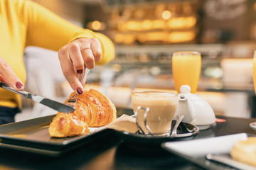 Couple having a breakfast at cafe, she is eating a croissant, both are drinking an orange juice.