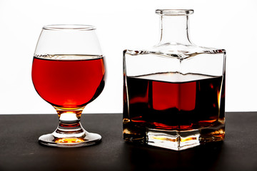 A glass of whiskey with ice or brandy and a square carafe on a black dish isolated against a white background. Whiskey with ice in the glass on a white background.