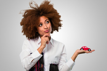 young afro woman holding a car toy and thinking