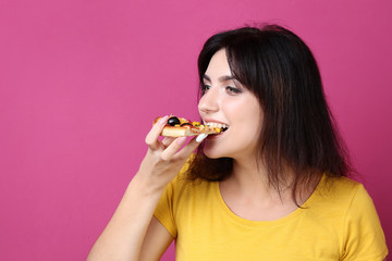 Young woman eating pizza on pink background