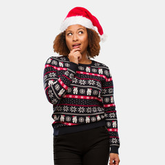 Young black woman in a trendy christmas sweater with print doubting and confused