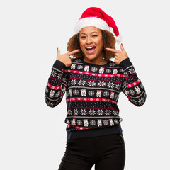 Young black woman in a trendy christmas sweater with print smiles, pointing mouth