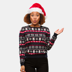 Young black woman in a trendy christmas sweater with print holding something on palm hand