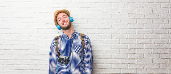 Young traveler man wearing backpack and a vintage camera cheerful and with a big smile, confident, friendly and sincere, expressing positivity and success. Listening to music with headphones.