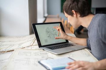 young male architector work with paper drawings and a laptop b