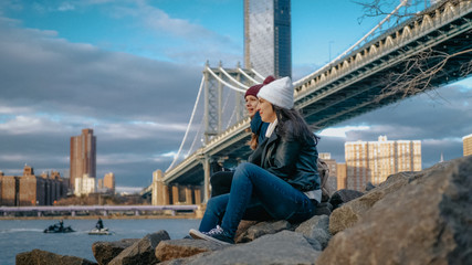 Two girls sit at Manhattan Bridge and enjoy their sightseeing trip to New York