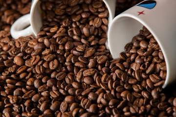 white cups with a pattern and grains of coffee on a black background