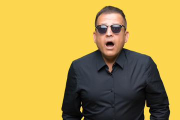 Middle age arab man wearing sunglasses over isolated background afraid and shocked with surprise expression, fear and excited face.