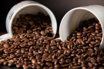 white cups with a pattern and grains of coffee on a black background