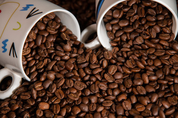 white cups with a pattern and grains of coffee on a black background