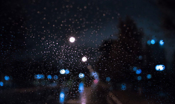 defocused. raindrops on a window at night. blurred city lights on the background. Rainy weather, reflected lights on a surface (asphalt)