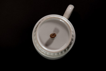 white cups with a pattern and grains of coffee on a black background