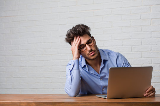 Young business man sitting and working on a laptop worried and overwhelmed, forgetful, realize something, expression of shock at having made a mistake