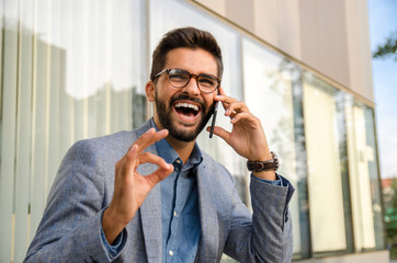 Happy businessman talking on phone and showing ok hand gesture 