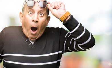 Handsome senior man wearing winter sweater and sunglasses afraid and shocked with surprise...