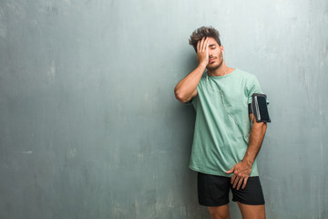 Young fitness man against a grunge wall worried and overwhelmed, forgetful, realize something, expression of shock at having made a mistake. Wearing an armband with phone.