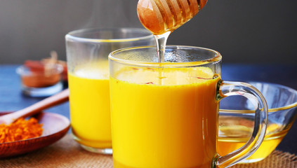 Sweetening saffron turmeric golden milk with honey. Honey is dripping from a wooden dipper in steaming  turmeric golden milk
