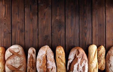 Assortment of baked bread and bread rolls on wooden table background